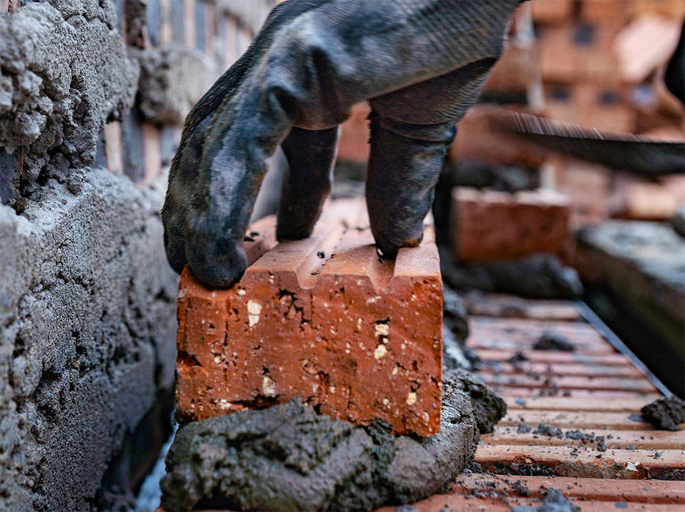 Masonry worker constructing load-bearing walls using concrete blocks and professional masonry tools.