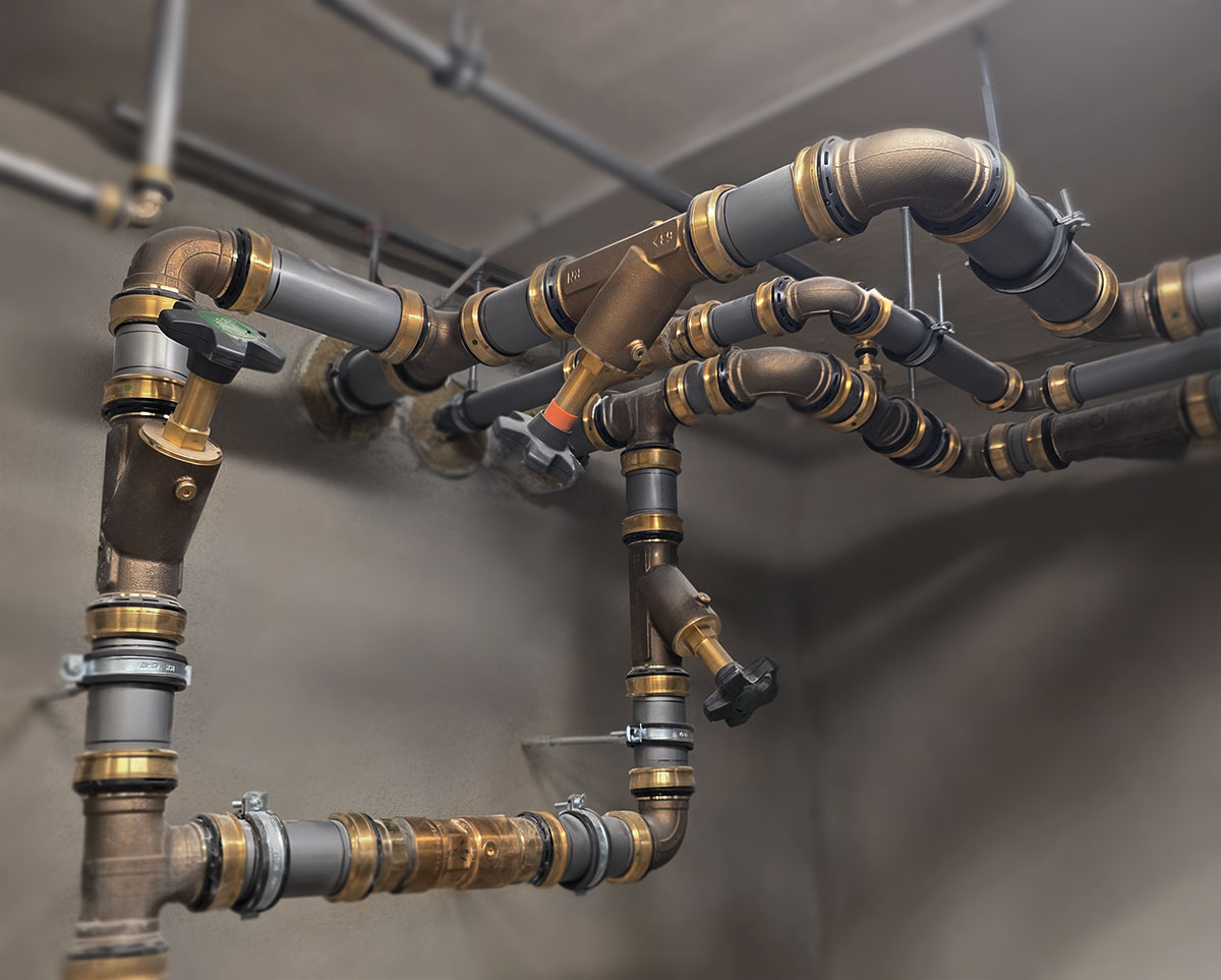 Dense installation of plumbing and heating pipes with valves, gauges and connections running along a technical corridor wall.