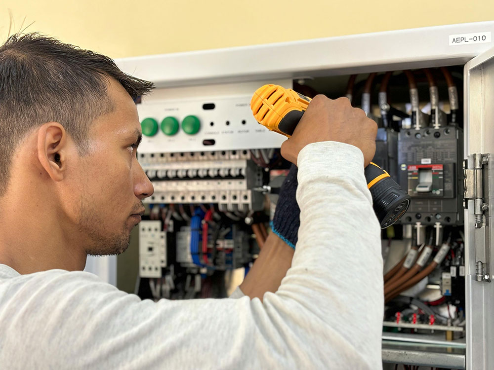 Electrician working inside electrical control panel using insulated screwdriver during installation