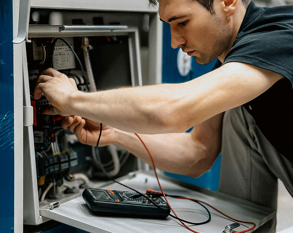 Electrician testing electrical connections with multimeter inside industrial control cabinet