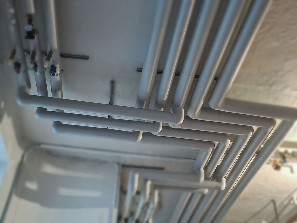 Parallel insulated water and heating pipes with Isover insulation and Isogen plastic finish, neatly routed along ceiling.
