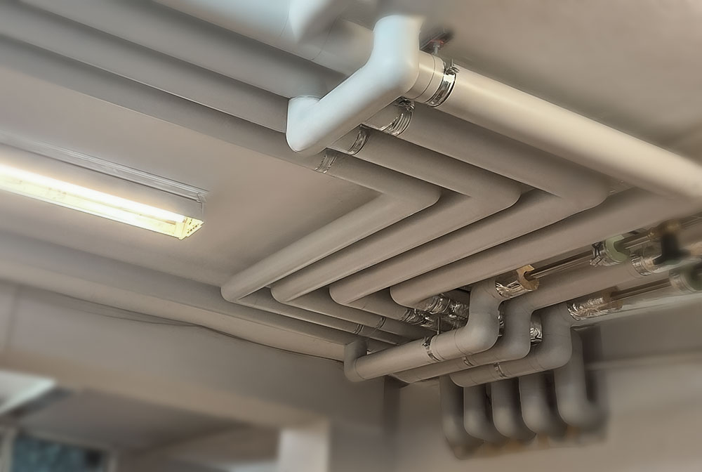 Plumbing pipe insulation with Isover and Isogen cladding, including sealed bends and fittings mounted under concrete slab.