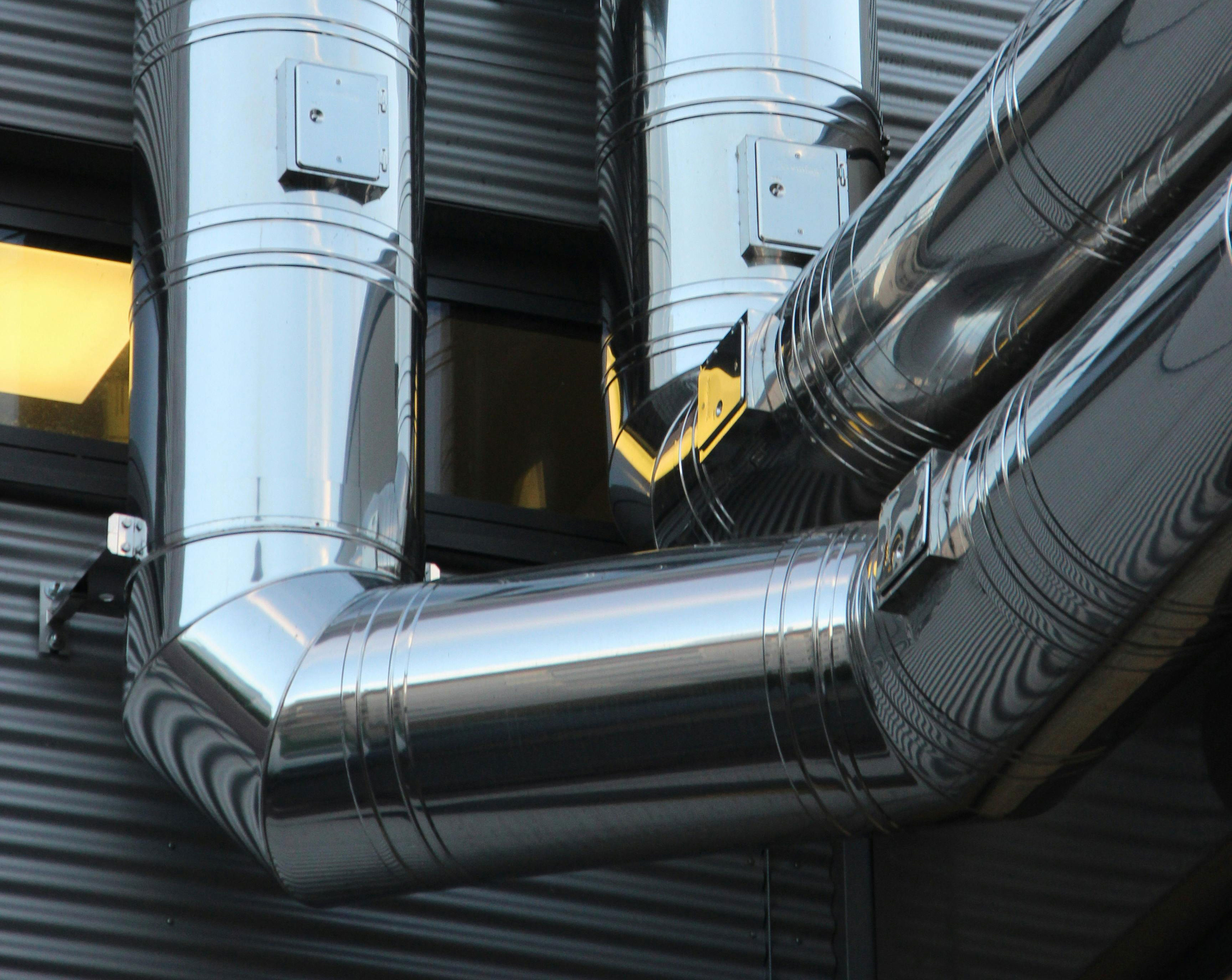 Shiny metal ventilation pipes installed on an exterior wall for an HVAC air system.