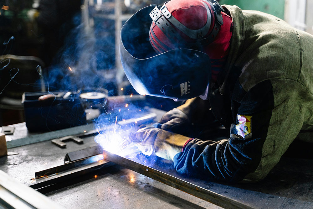 Welder performing arc welding on steel profiles in an industrial workshop