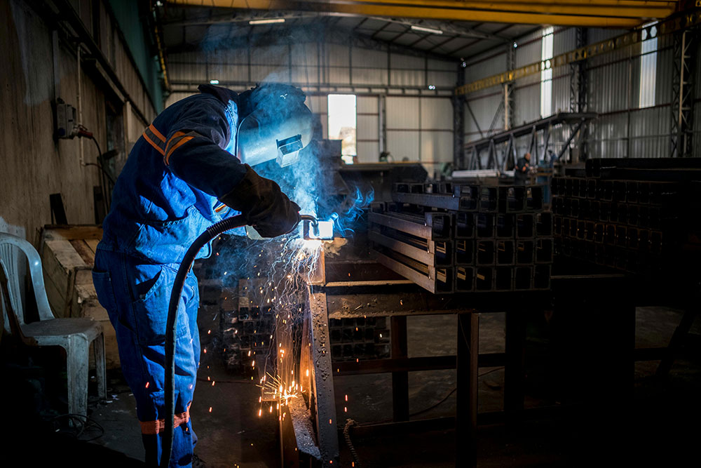 Industrial welder welding steel components inside a metal fabrication hall