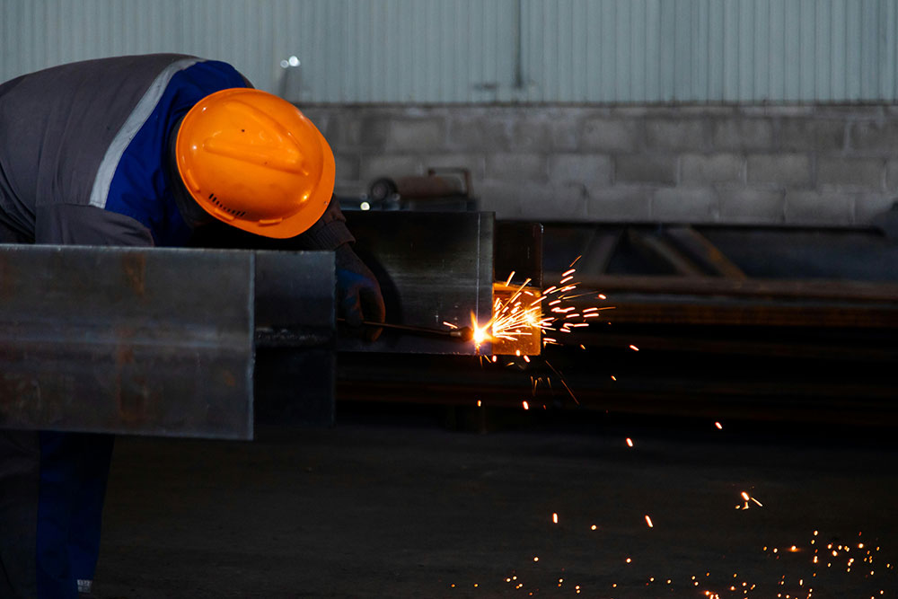 Welder manually welding steel beams with protective equipment